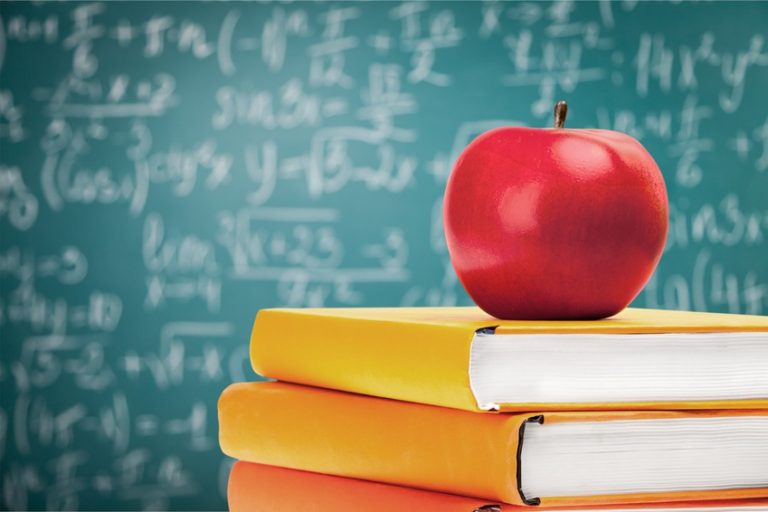 Apfel auf einem Bücherstapel vor einer Tafel mit Formeln