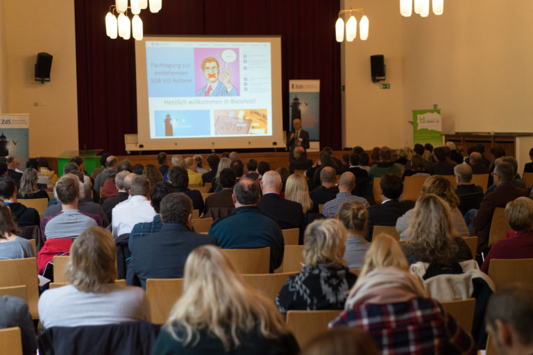 Publikum im Saal vor einer Präsentationsleinwand