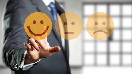 Mann im Anzug hält drei Smileys: fröhlich, neutral, traurig
