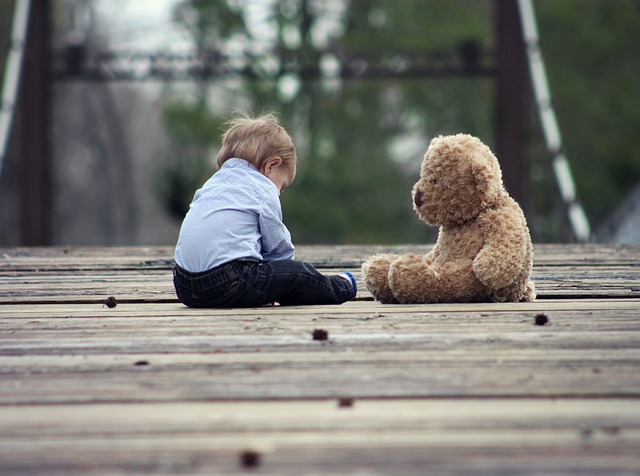 Kleines Kind sitzt mit einem Teddybär auf einem Holzsteg