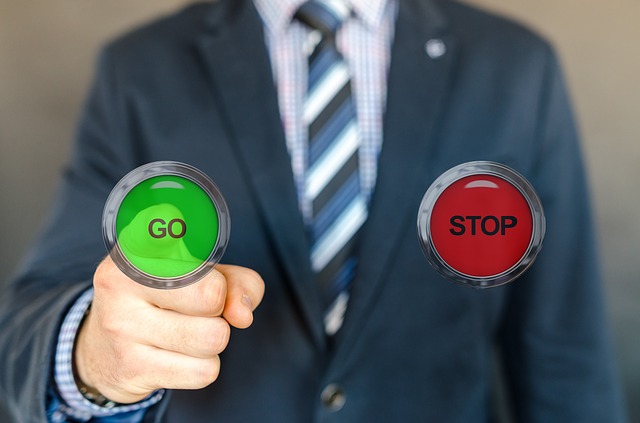 Mann im Anzug hält einen grünen „Go“- und einen roten „Stop“-Knopf