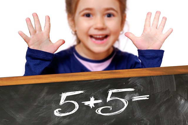 Mädchen hebt die Hände hinter einer Tafel mit der Rechnung „5+5=“