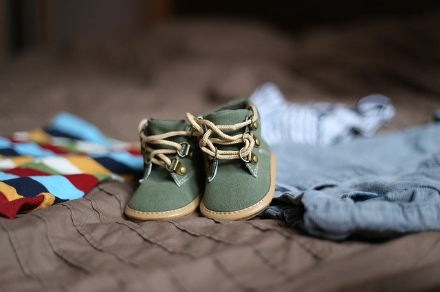 Kinderschuhe und Kleidung auf einem Bett