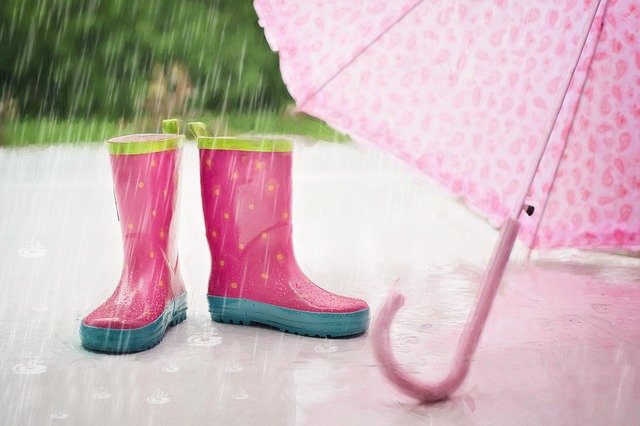 Rosa Gummistiefel und Regenschirm auf nassem Boden