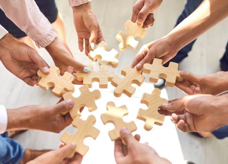Viele Hände legen gemeinsam ein Puzzle zusammen
